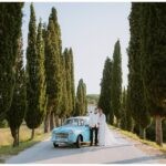 Brautpaar in weiß und einen Türkisblauen Oldtimer auf einen abgelegenen Gehweg mit Bäumen bei ihrer Hochzeit in Istrien Kroatien